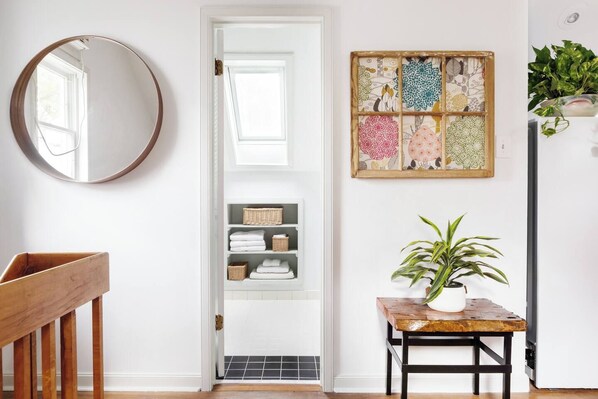A hallway with a wooden bench, a mirror, a door with a window, a shelf with folded towels, and a wall-mounted plant.