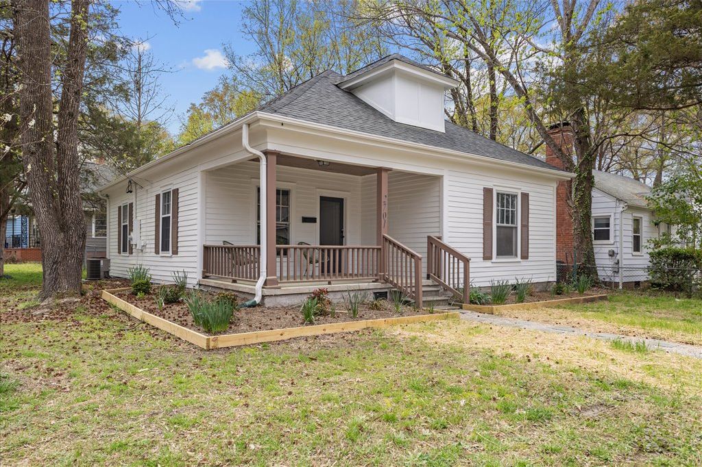 A single-story house with a front porch, a chimney, and a small garden area.