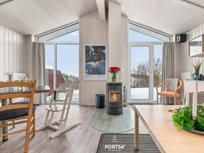A modern interior with a wood-burning stove, large windows, and a dining area. - Holiday Home With 1 Bedroom (Braunlage)