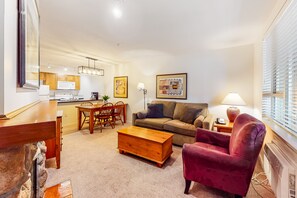 Una sala de estar con sofá, sillón, mesa de centro, mesa de comedor y cocina al fondo.
