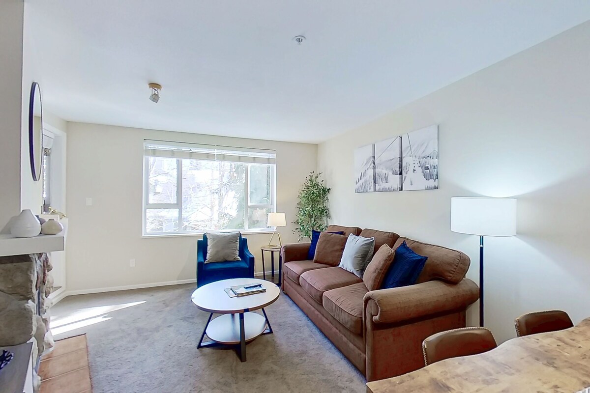 A living room with a brown sofa, blue armchairs, a round coffee table, and a large window.
