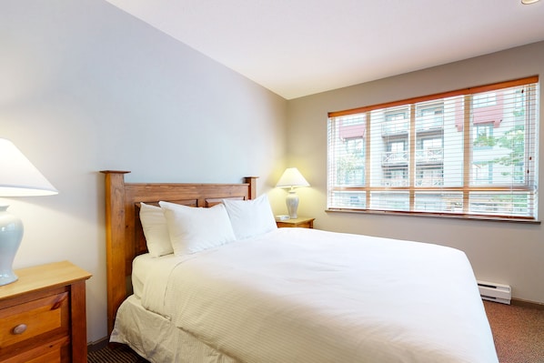 A neatly made bed with white linens, a wooden headboard, and two bedside lamps.