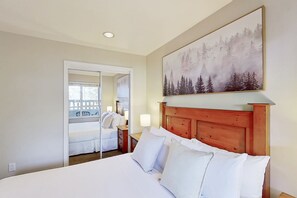 A hotel room with a large bed, a wooden headboard, a painting of a forest, and a mirror reflecting the room.