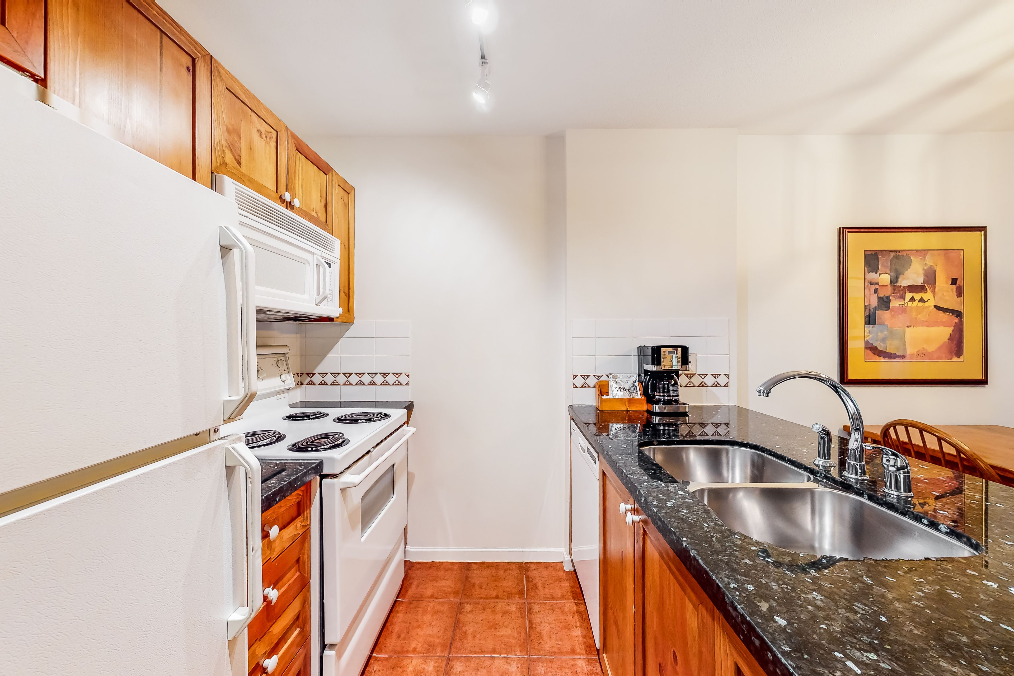 A compact kitchen with white appliances, wooden cabinets, a granite countertop, and a tiled backsplash.