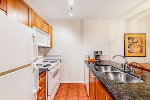 A compact kitchen with white appliances, wooden cabinets, a granite countertop, and a tiled backsplash.