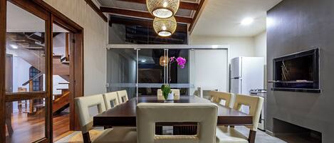 A dining area with a wooden table and chairs, a chandelier, and a kitchen with a refrigerator and stove.