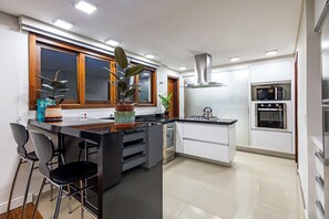 Une cuisine moderne dotée d’un îlot central, de tabourets de bar, d’une cuisinière, d’un four à micro-ondes et d’une hotte en acier inoxydable.