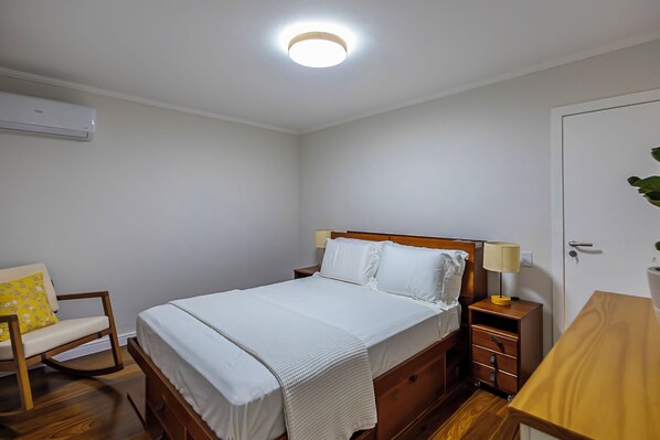 A bedroom with a bed, bedside table, chair, and a door.
