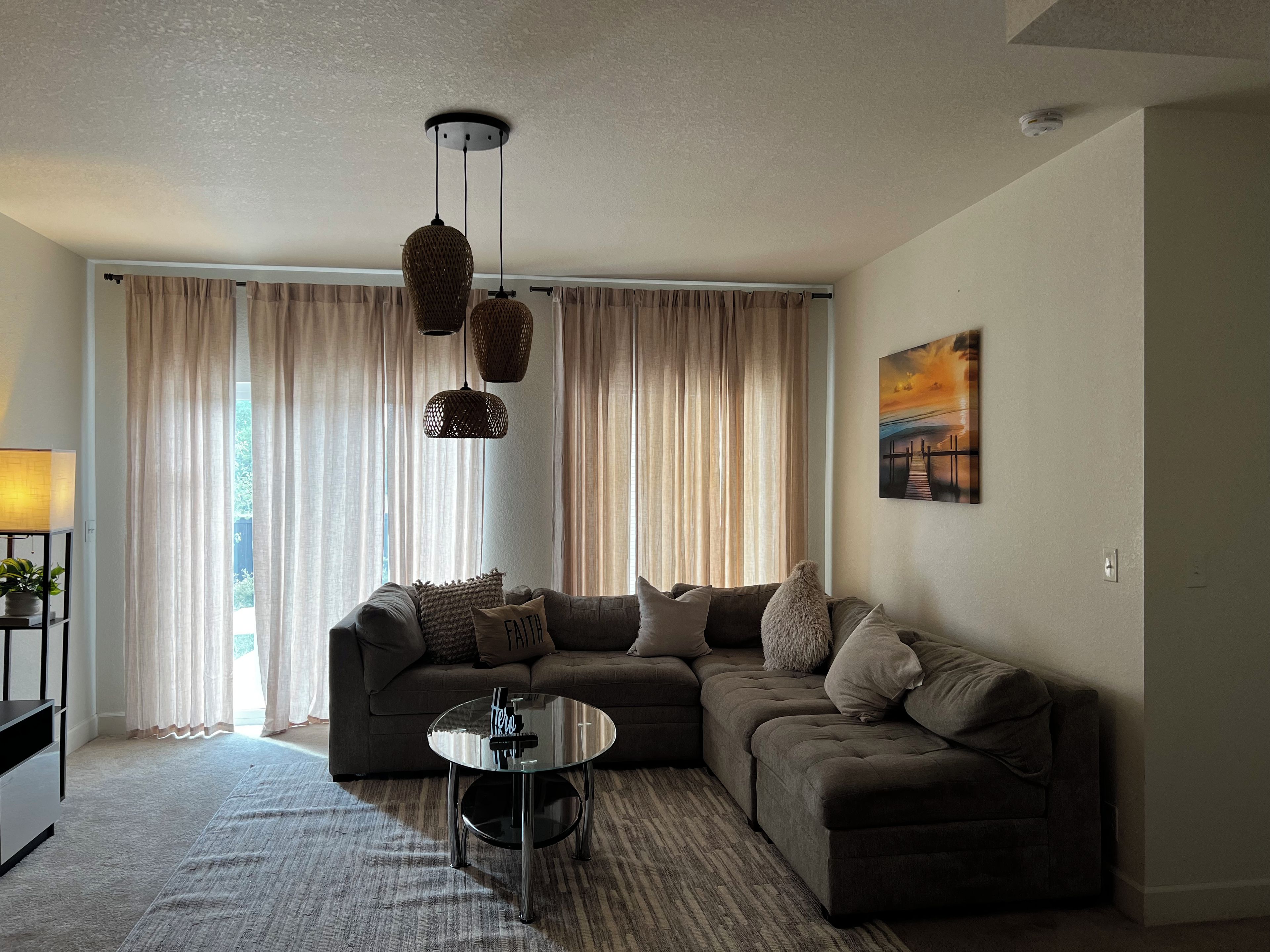 A living room with a sectional sofa, a glass coffee table, and a hanging light fixture.