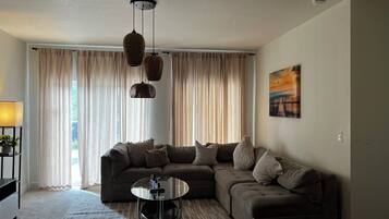 A living room with a sectional sofa, a glass coffee table, and a hanging light fixture.
