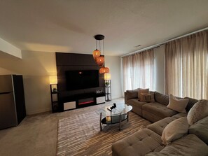 Ein modernes Wohnzimmer mit Flachbildfernseher, einer Couch, einem Couchtisch und einem gemusterten Teppich.