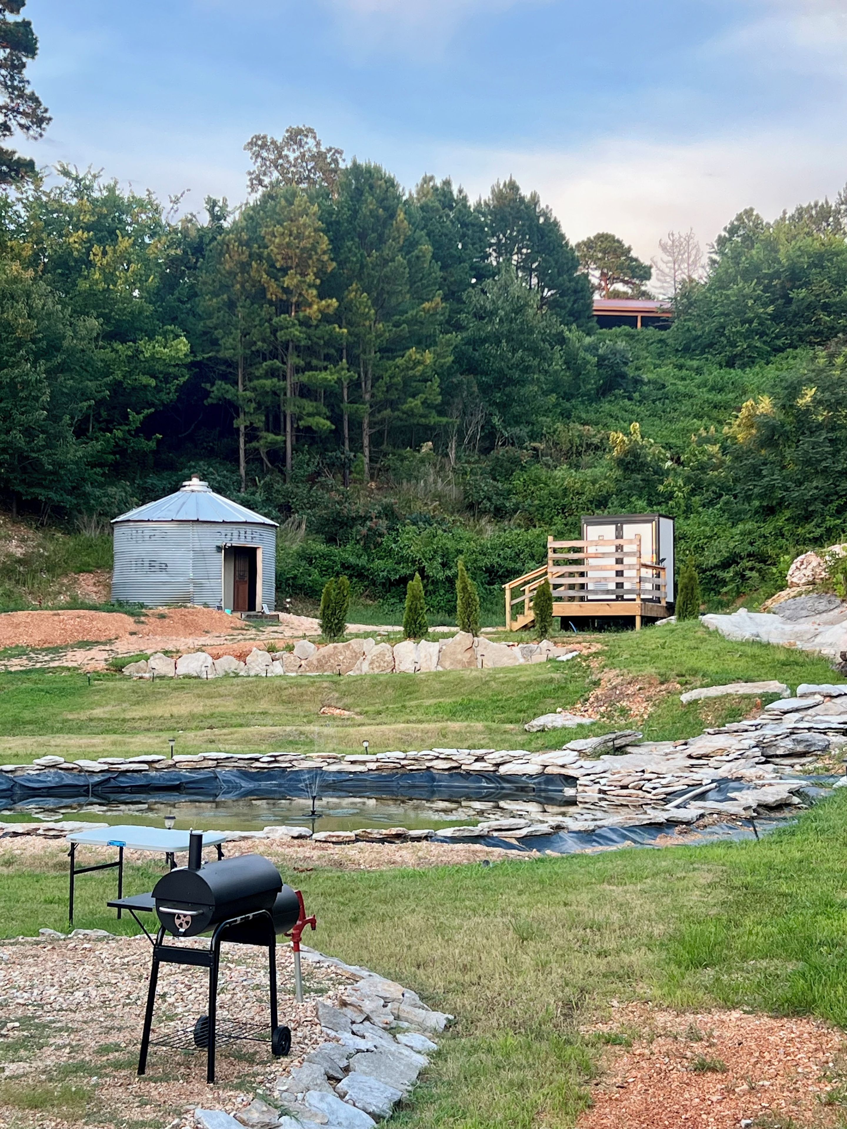 A rustic outdoor setting with a small shed, a grill, and a pond.