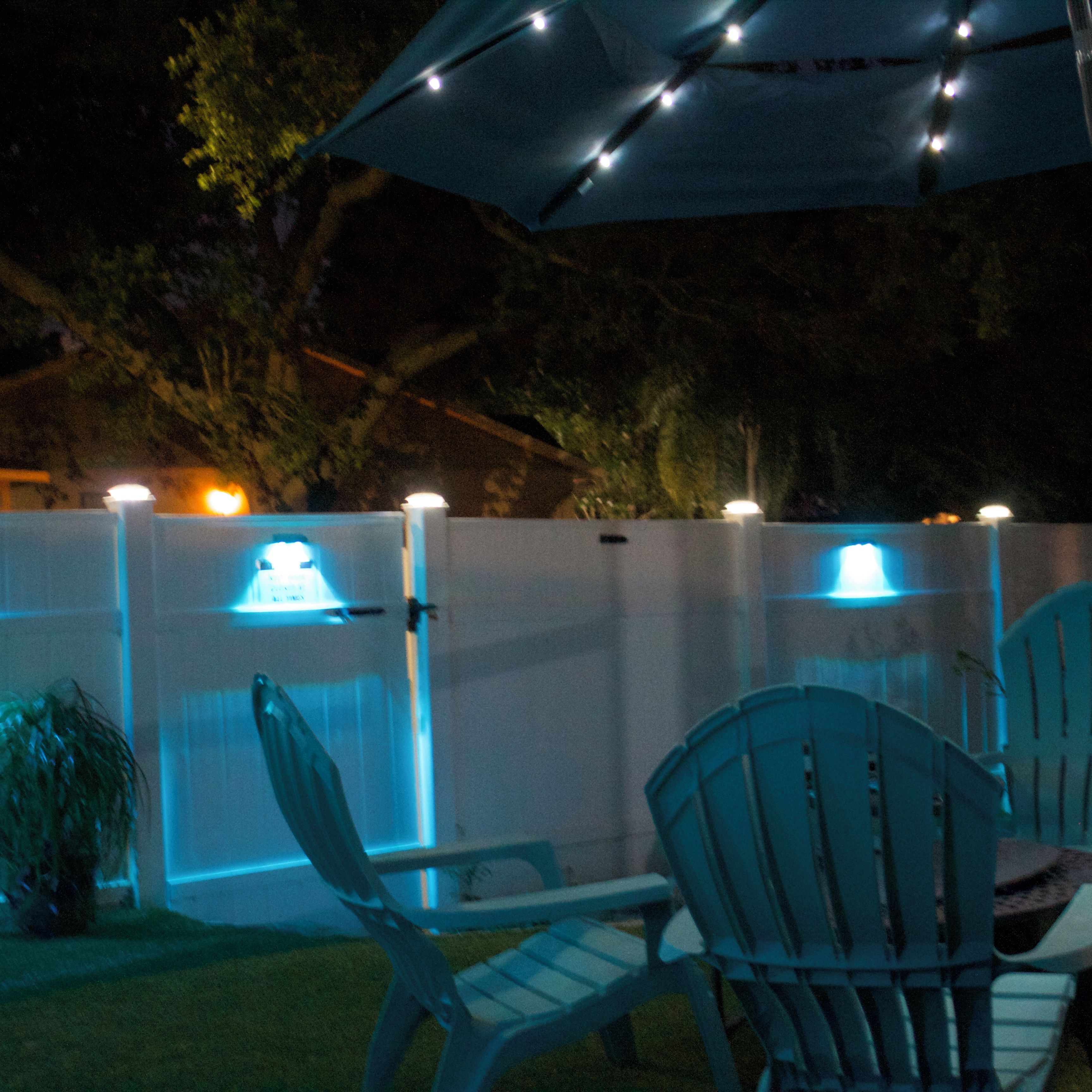 Un espace extérieur aménagé avec des chaises et un parasol, entouré d’une clôture blanche agrémentée de guirlandes lumineuses.