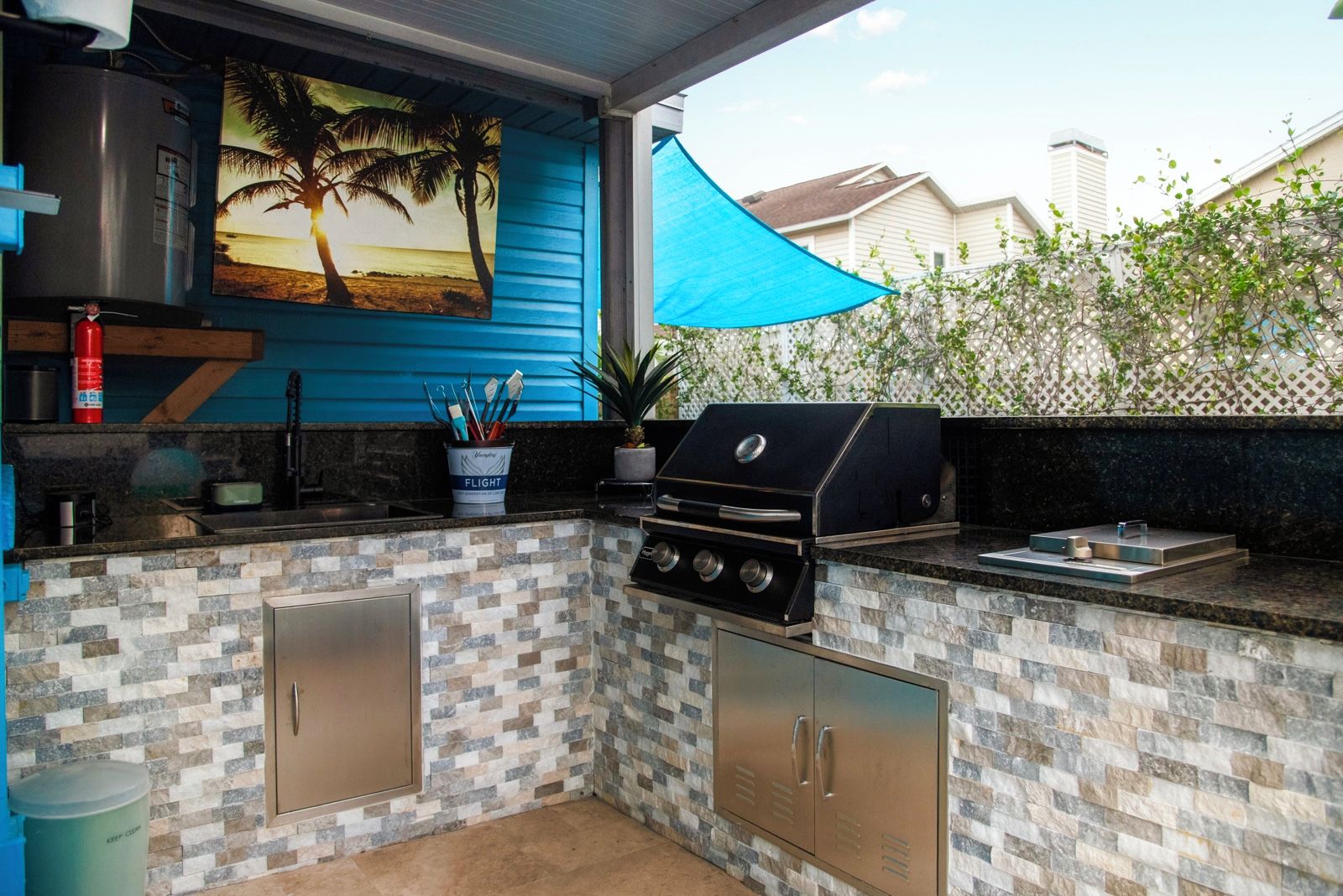 An outdoor kitchen with a grill, a sink, and a cabinet.