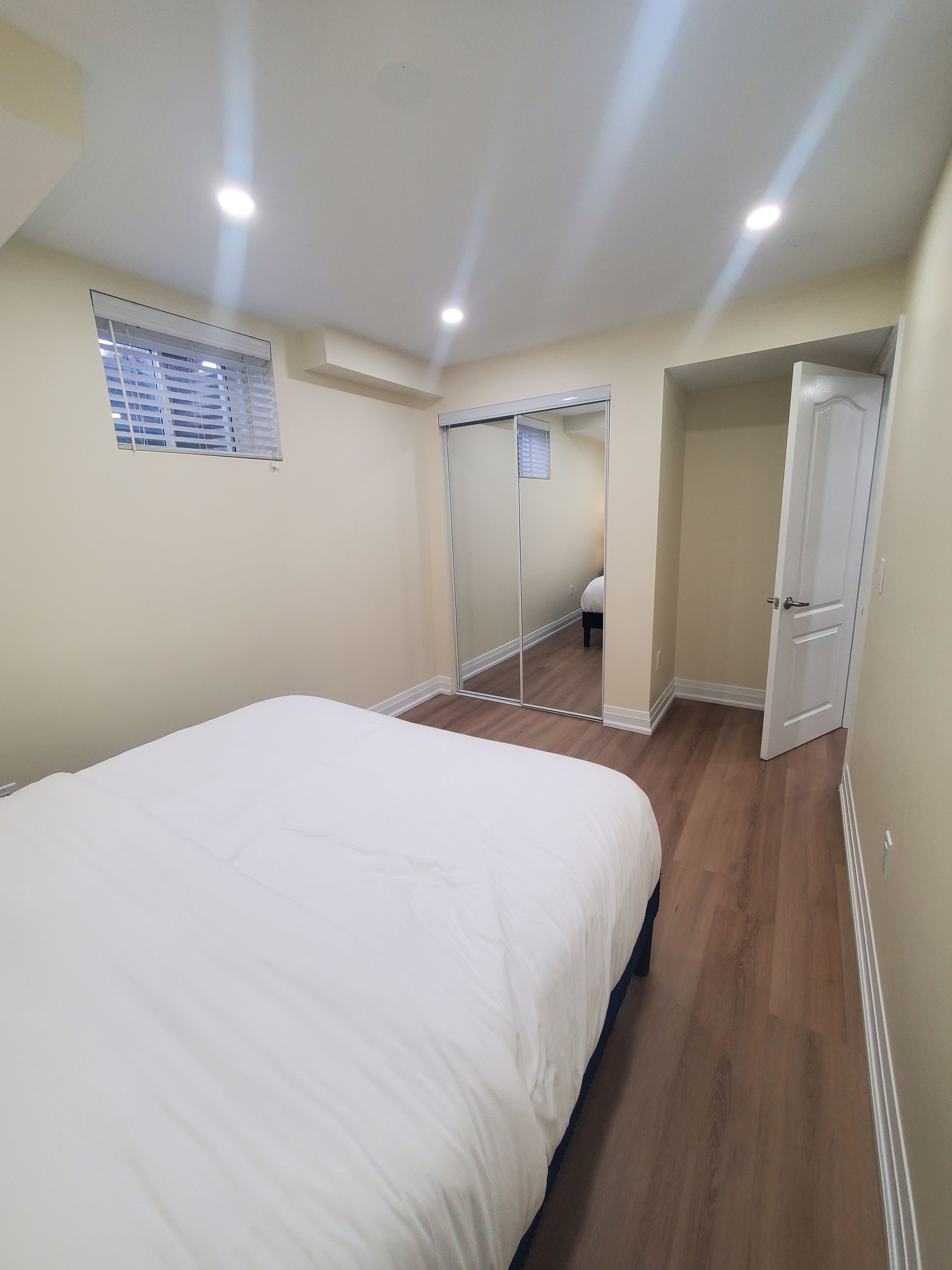 A bedroom with a large bed, a wardrobe, a mirror, and a door leading to another room.