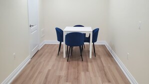 Een kamer met een witte tafel en vier blauwe stoelen, houten vloeren en inbouwspots.