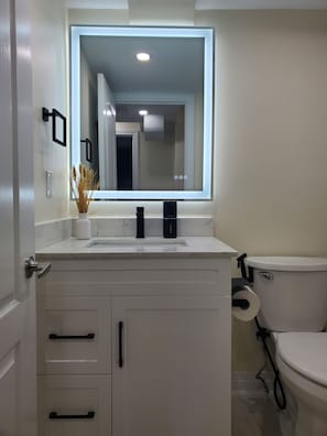 Une salle de bain avec un lavabo blanc, un miroir, des toilettes et un meuble avec des tiroirs.