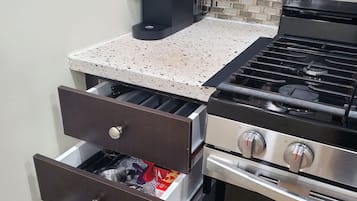 A kitchen with a coffee maker, a stove, and drawers containing kitchen utensils and packaged food.