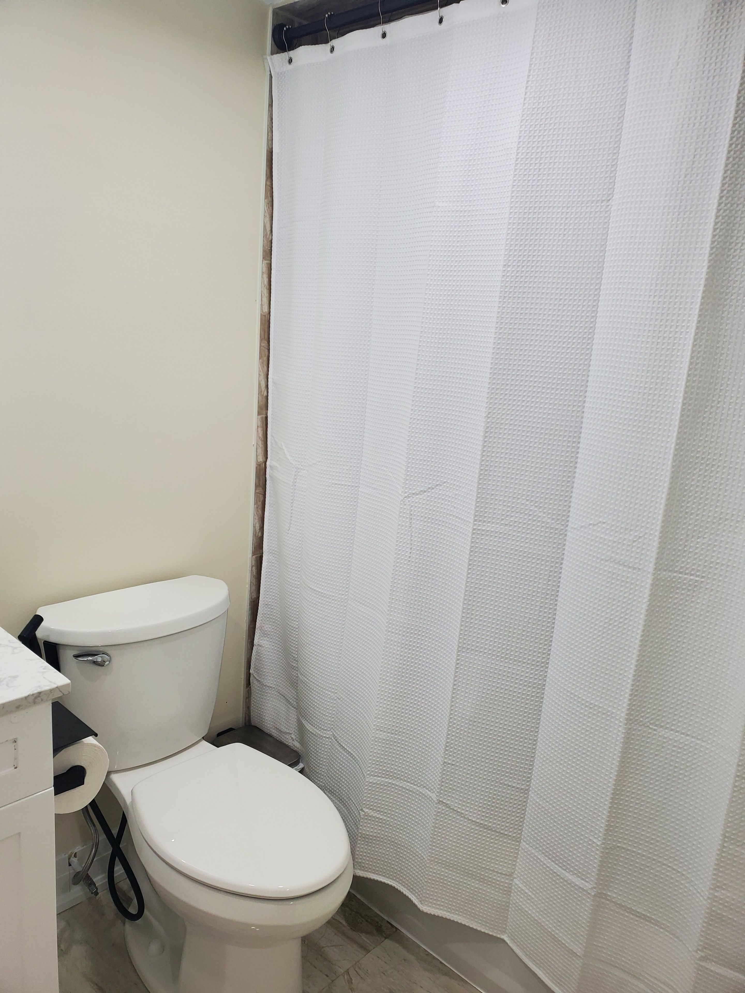 A bathroom with a toilet, a shower curtain, and a marble countertop.