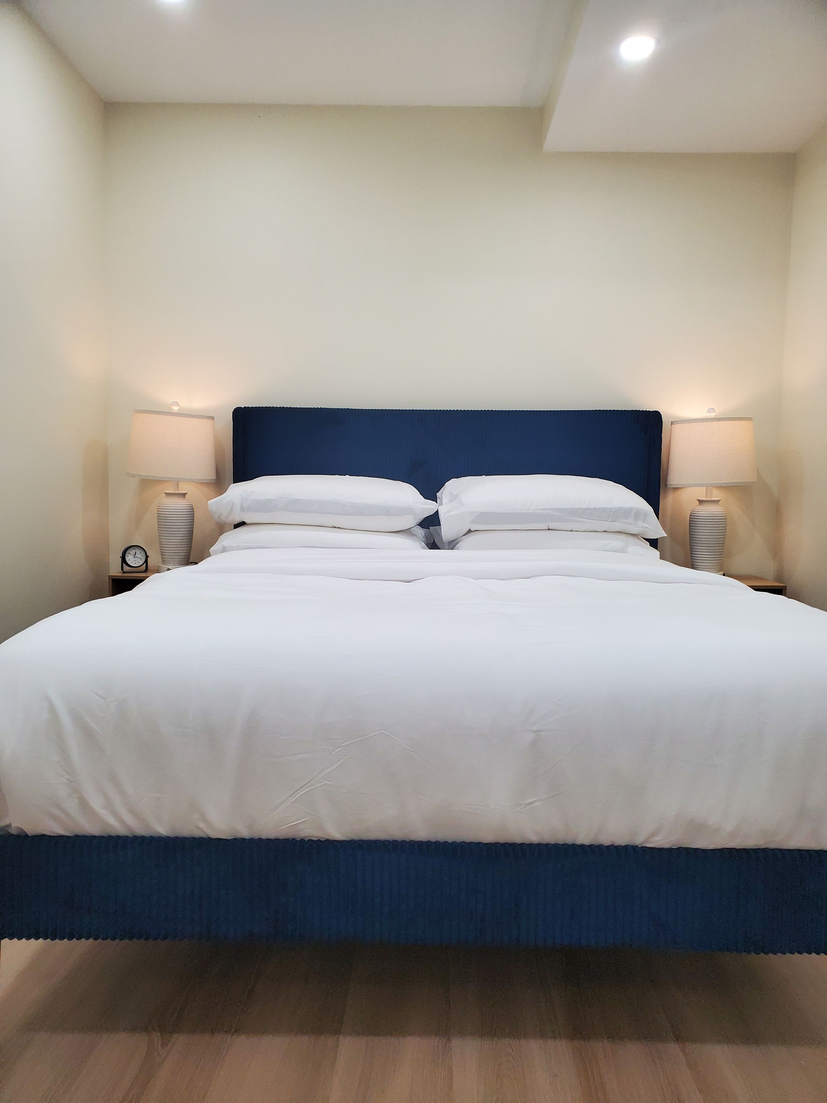 A neatly made bed with white linens and a blue headboard, flanked by two bedside lamps.