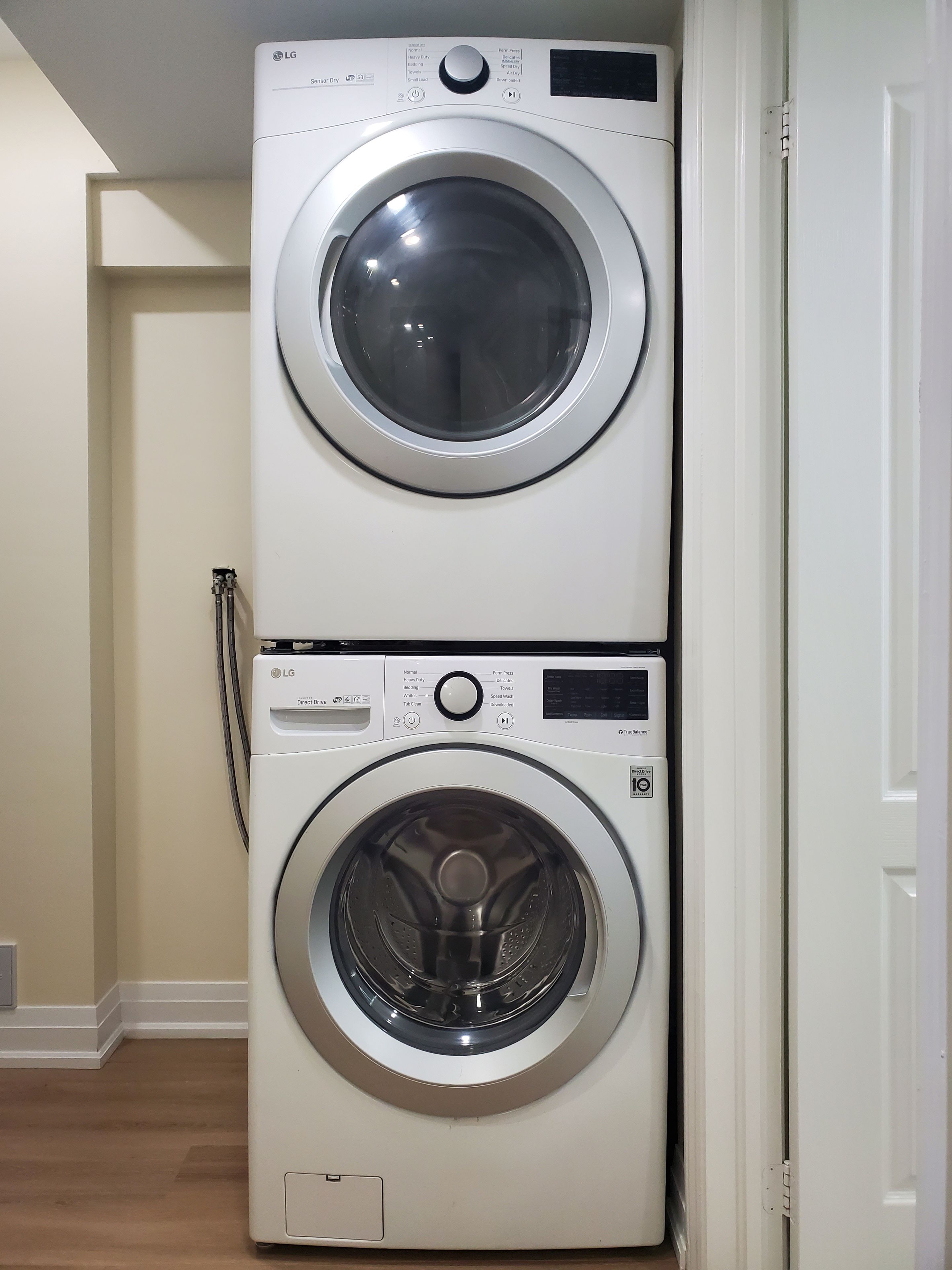 A stacked washer and dryer unit in a room with a wooden floor and a white door.