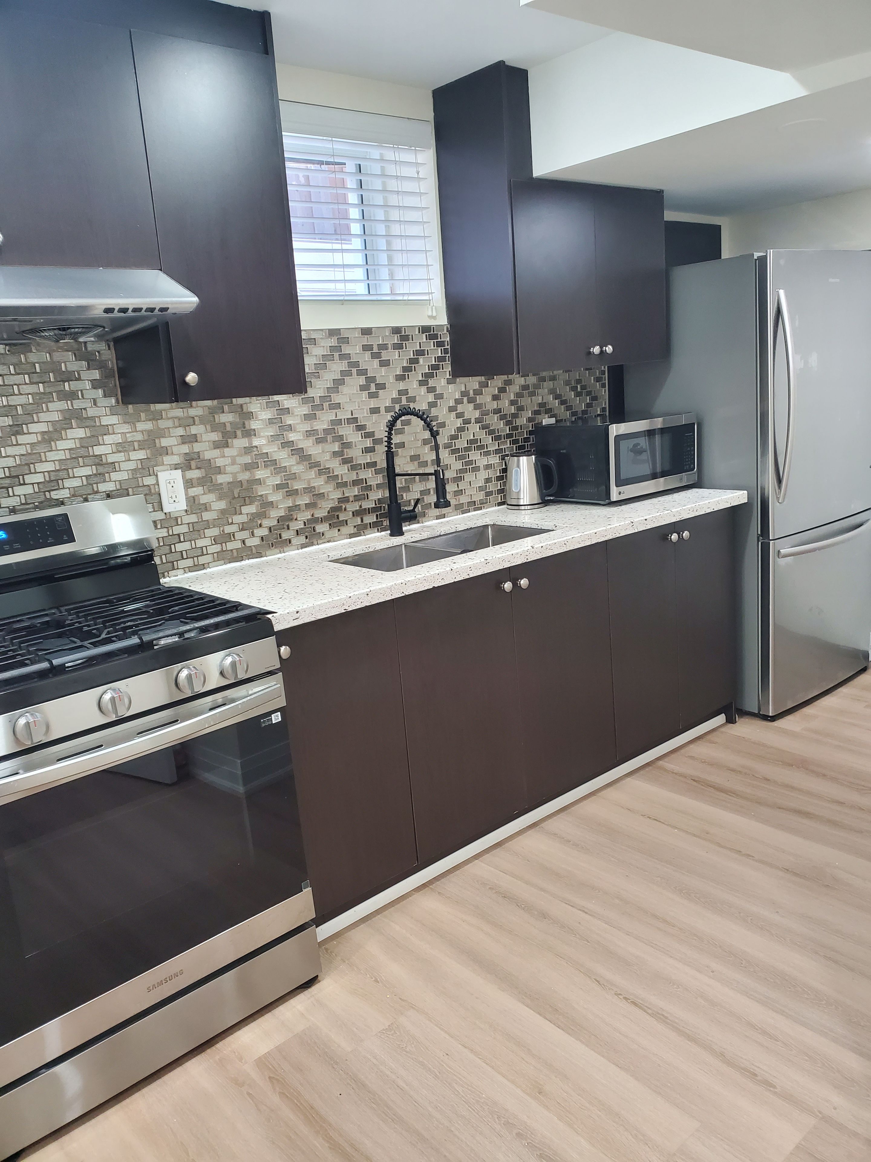 Una cocina moderna con armarios oscuros, un refrigerador de acero inoxidable, un microondas y una estufa a gas.