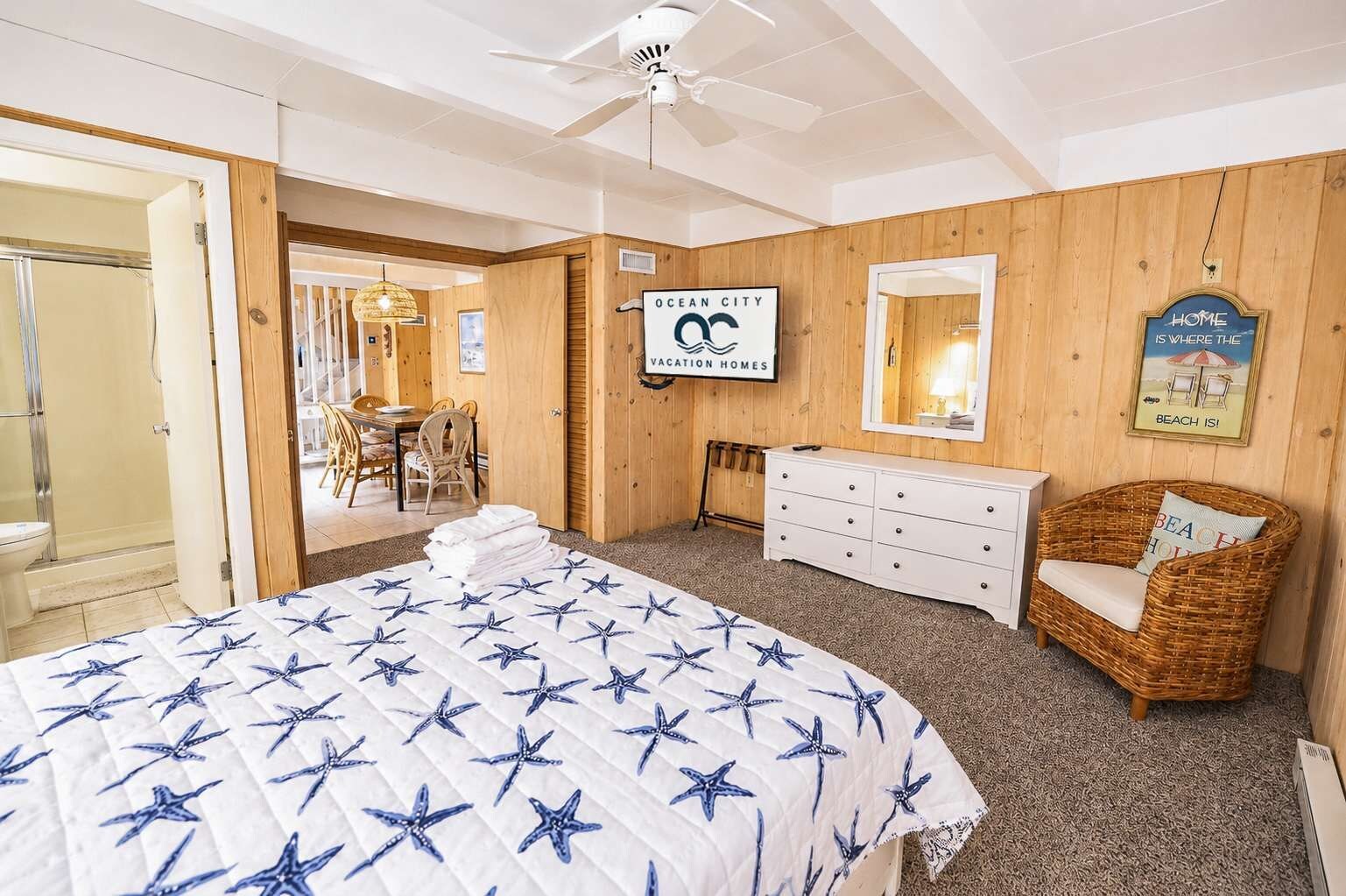 Een slaapkamer met een bed, een kaptafel, een rieten stoel, een spiegel en een bord met de tekst Ocean City Vacation Homes.