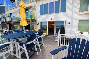 Eine Terrasse mit Tisch und Stühlen, einem gelben Sonnenschirm und einem Gebäude mit zahlreichen Fenstern und Balkonen.