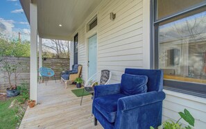 Eine überdachte Veranda mit blauem Stuhl, Korbstuhl und einem kleinen Tisch mit Pflanze.
