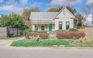 Ein eingeschossiges Haus mit grüner Tür, einer Veranda und einem Garten mit Kakteen und blühenden Pflanzen.