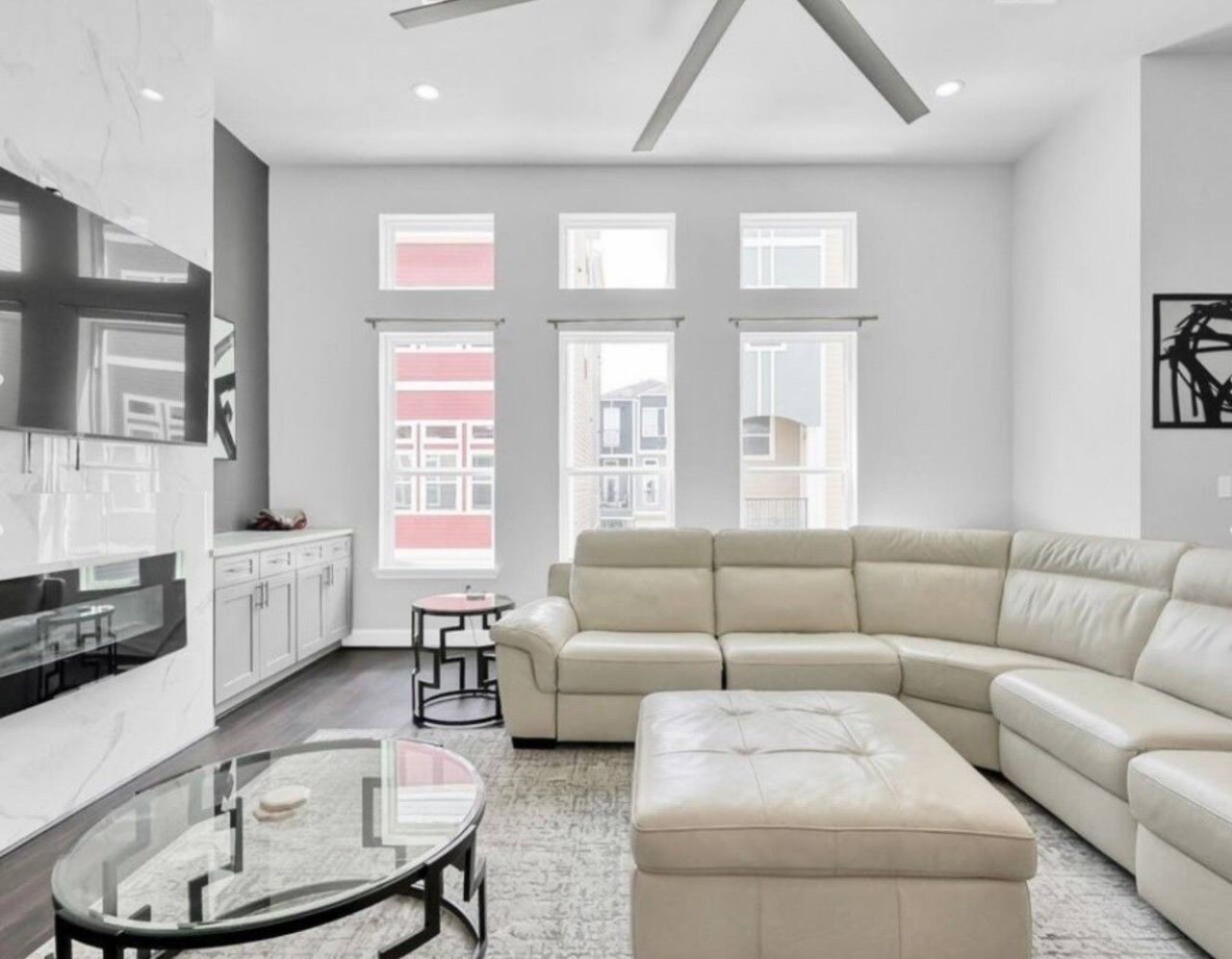 A modern living room with a sectional sofa, a glass coffee table, and a kitchen area with white cabinets and a marble countertop.