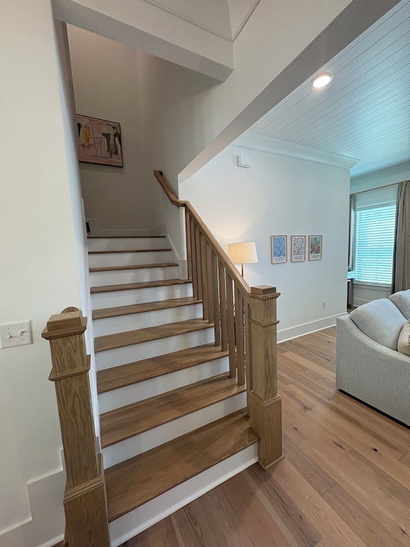 Una escalera con barandas de madera que conduce a un piso superior, una lámpara en el rellano y un sofá en la habitación contigua.
