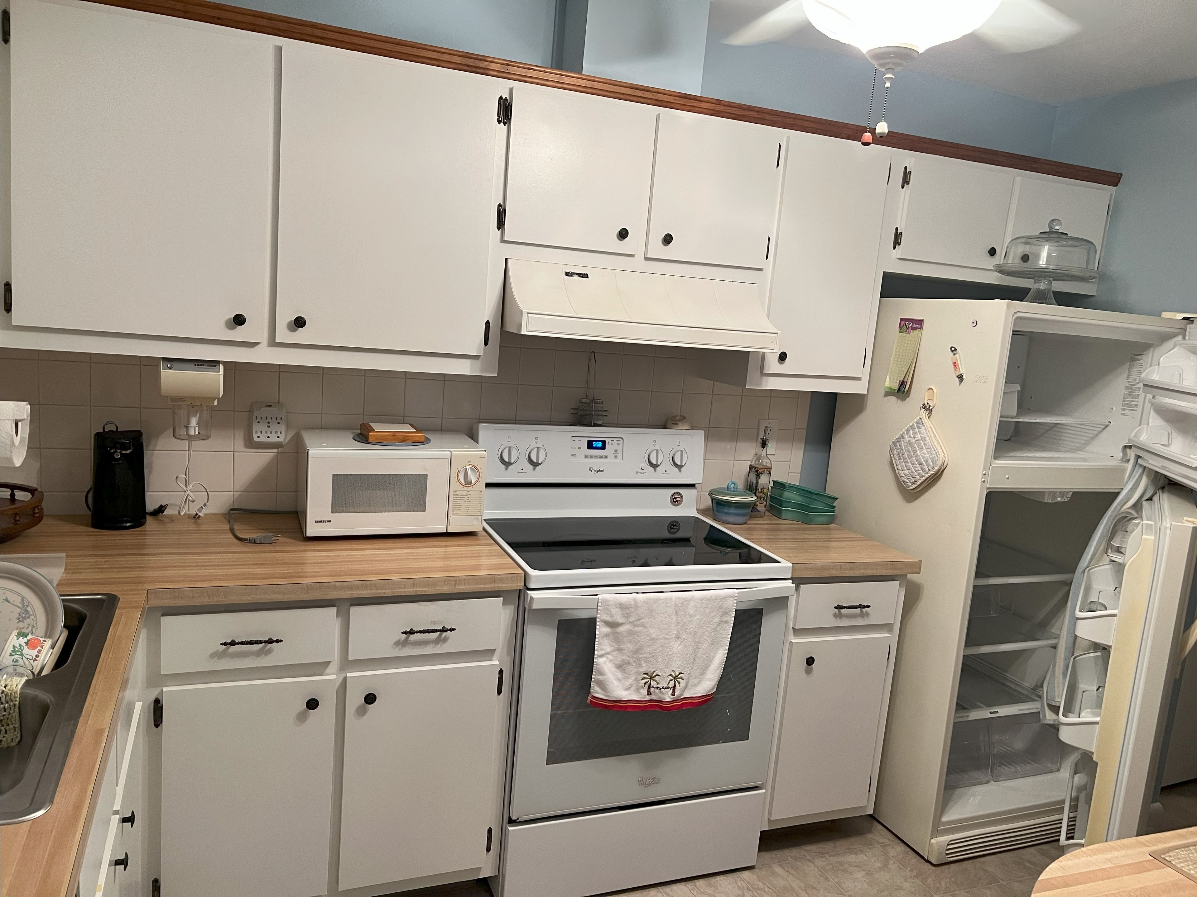 A kitchen with white cabinets, a microwave, an oven, a refrigerator, and a wooden countertop.
