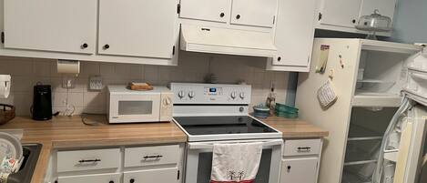 A kitchen with white cabinets, a microwave, an oven, a refrigerator, and a wooden countertop.
