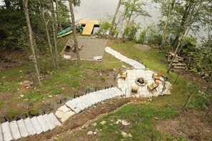Ein steinbelagter Weg führt zu einer Holzterrasse mit Feuerstelle und Sitzgelegenheiten.