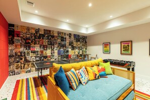 Ein Zimmer mit einem farbenfrohen Sofa, einem Tischtennis-Tisch und einer Wand, die mit verschiedenen Postern bedeckt ist.