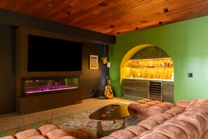 Ein modernes Wohnzimmer mit großem Flachbildfernseher, einer Bar mit grüner Wand und einem gemusterten Teppich.