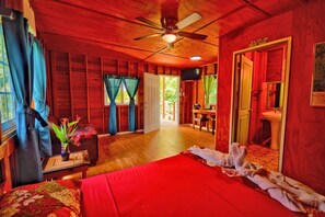 A room with a bed, a desk, a chair, a ceiling fan, and a door leading to another room. - Cozy Cabin on 30 Acre Avocado & Fruit Farm in San Ignacio, Cayo with Wifi & AC (San Ignacio)