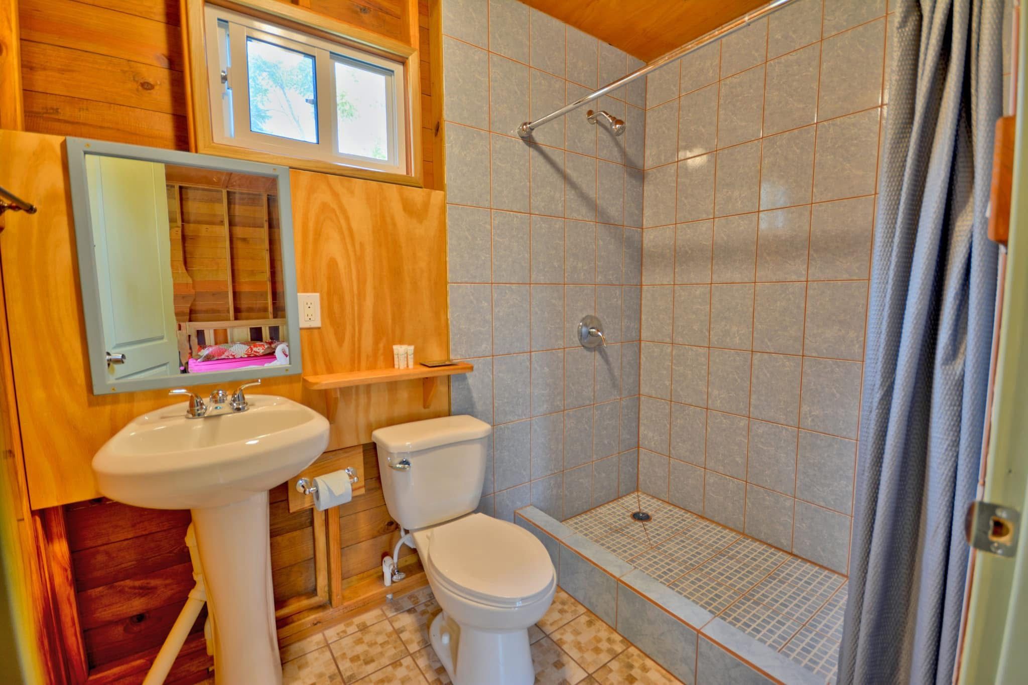 A bathroom with a shower, toilet, sink, and wooden paneling.