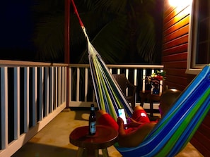 A hammock on a balcony with a bottle and a smartphone on a table. - Cozy Cabin on 30 Acre Avocado & Fruit Farm in San Ignacio, Cayo with Wifi & AC (San Ignacio)