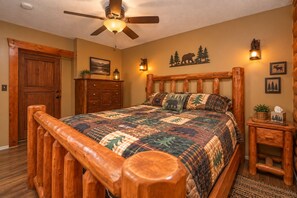 A bedroom with a wooden bed frame, a ceiling fan, a quilted bedspread, a wooden dresser, and wall-mounted lights.