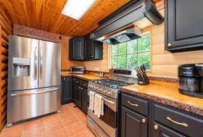 A modern kitchen with stainless steel appliances, a built-in oven, and a window with a view of greenery.