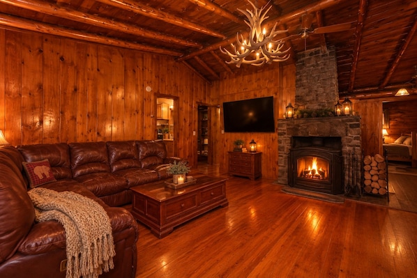 A log cabin interior with a leather sofa, a fireplace, a television, and wooden walls.