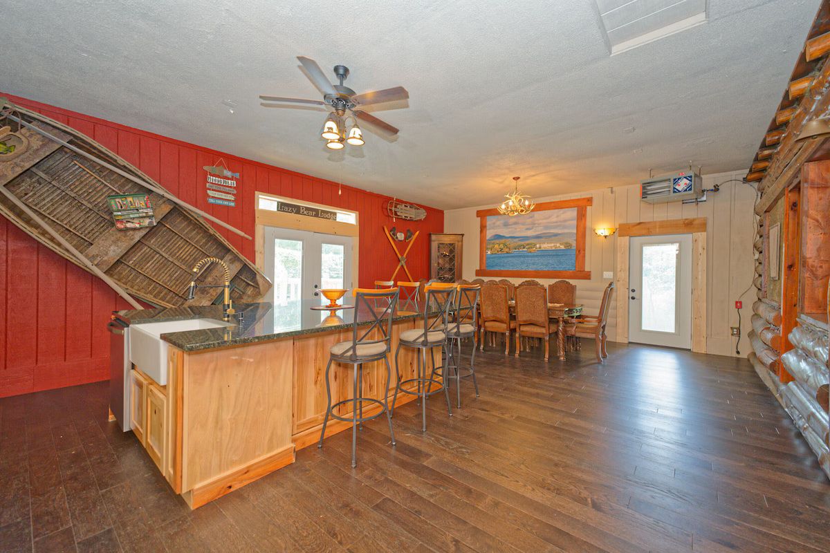 A kitchen with a wooden island, bar stools, a ceiling fan, and a dining area with chairs.