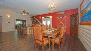 A dining area with a wooden table and chairs, a chandelier, and a red wall with a door labeled 'Mary Bear Lodge'. - Black Bear Lodge -Spacious 4BR in Prime LG Location! (Lake George)