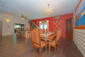 Een eetgedeelte met een houten tafel en stoelen, een kroonluchter, en een rode muur met een deur waarop 'Mary Bear Lodge' staat.