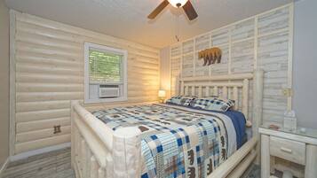 A bedroom with a wooden log wall, a bed with a blue and white checkered bedspread, a ceiling fan, and a window with blinds.