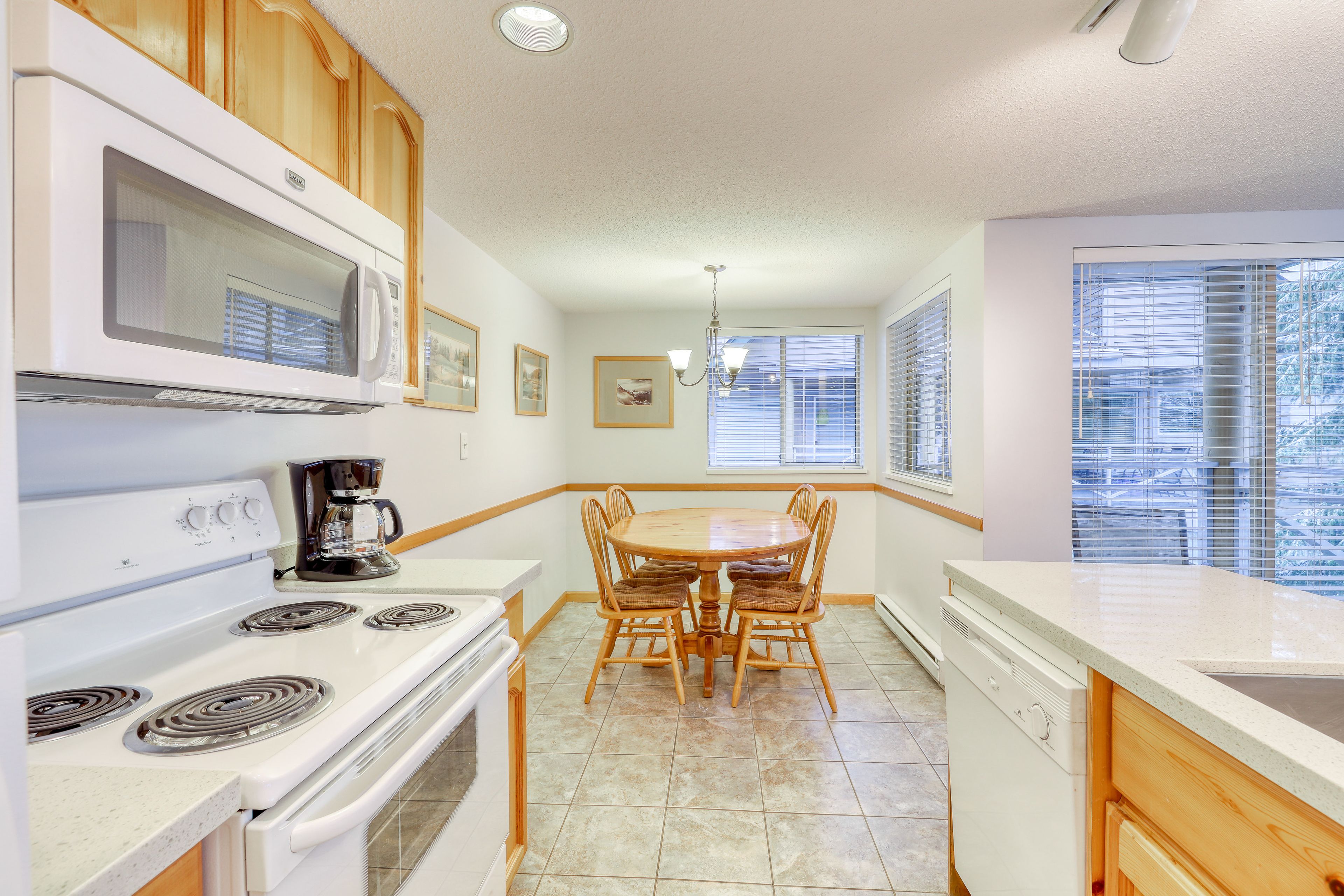 A kitchen with wooden cabinets, a white stove, a microwave, a dining table with chairs, and a window with blinds.