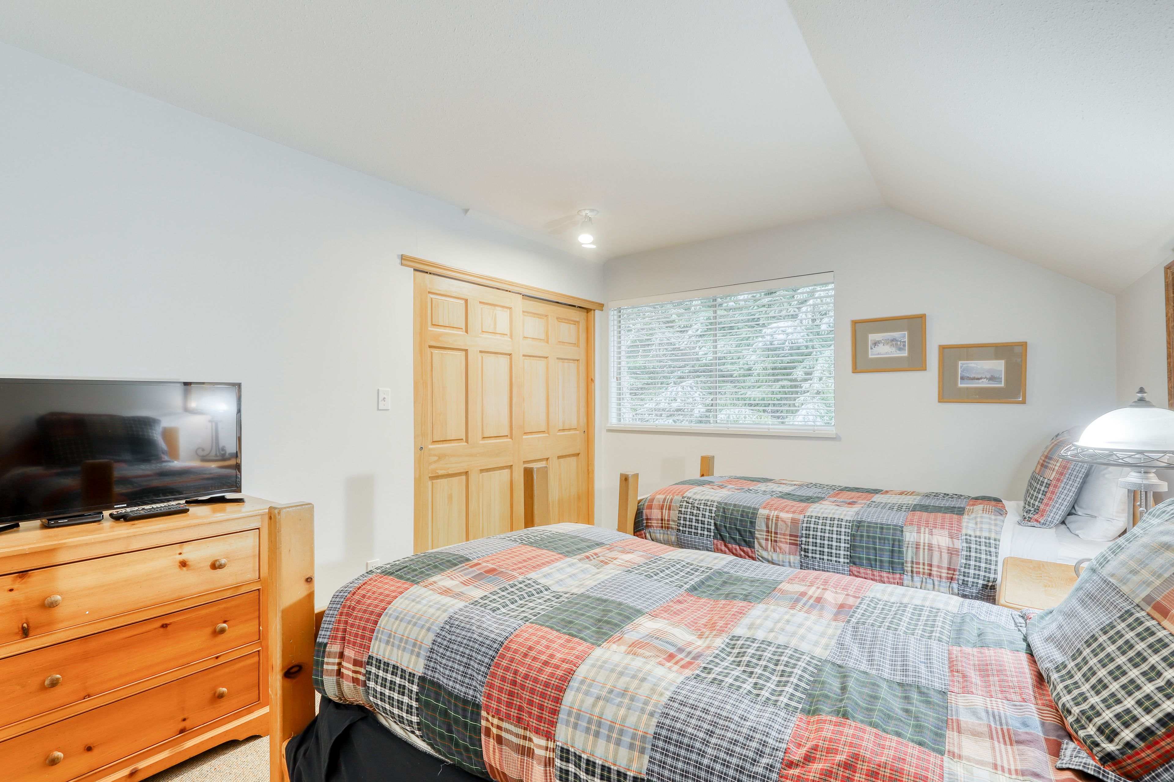 Quarto com duas camas, penteadeira de madeira, televisão e janela com cortinas.
