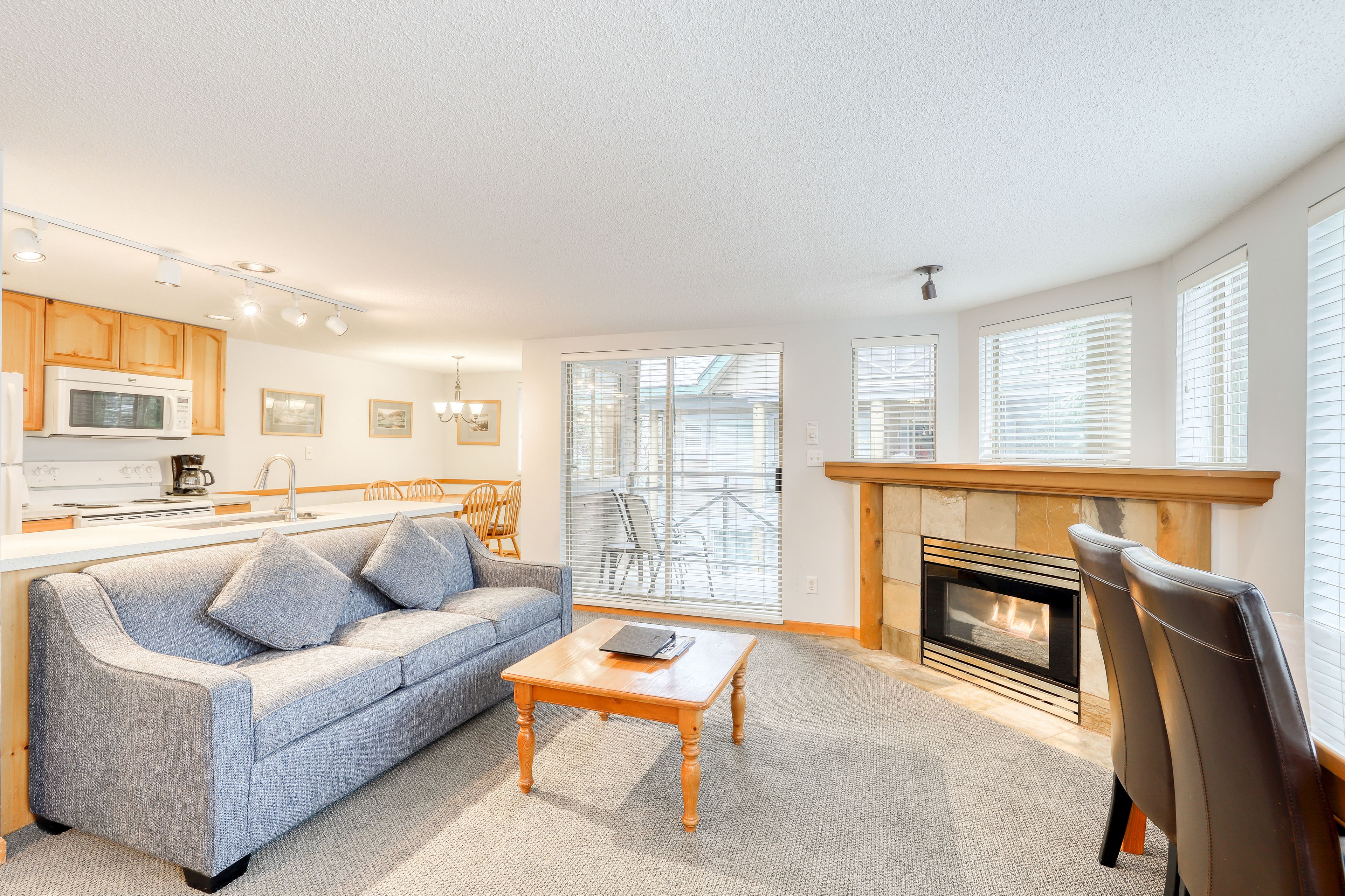 A modern living room with a sofa, coffee table, fireplace, and kitchen area with wooden cabinets and a microwave.